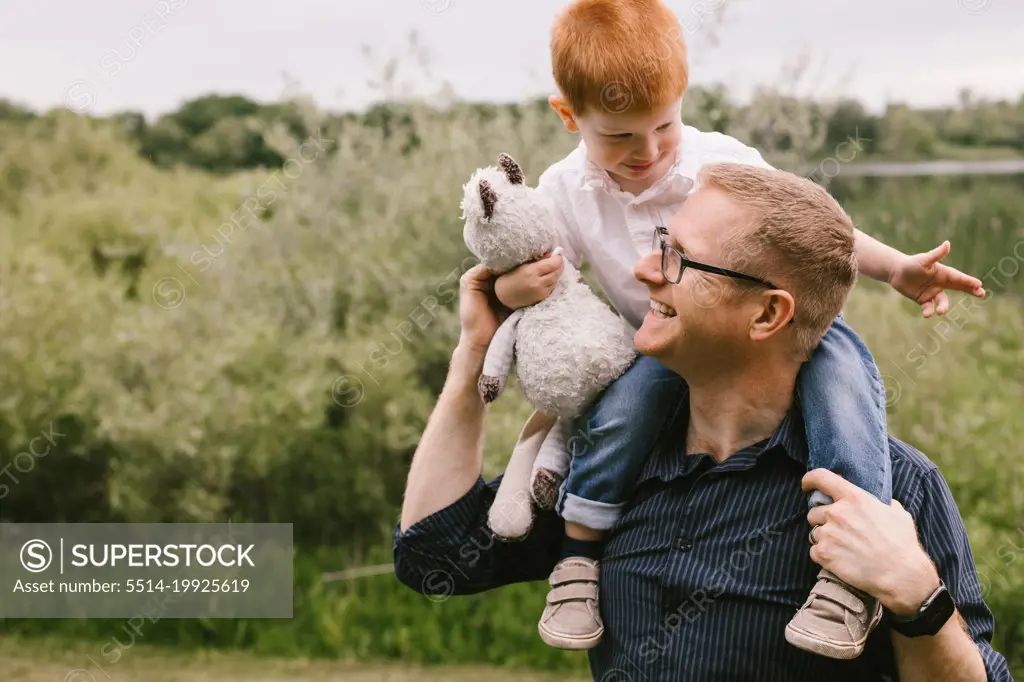 Son sits on dads shoulders while they smile and laugh