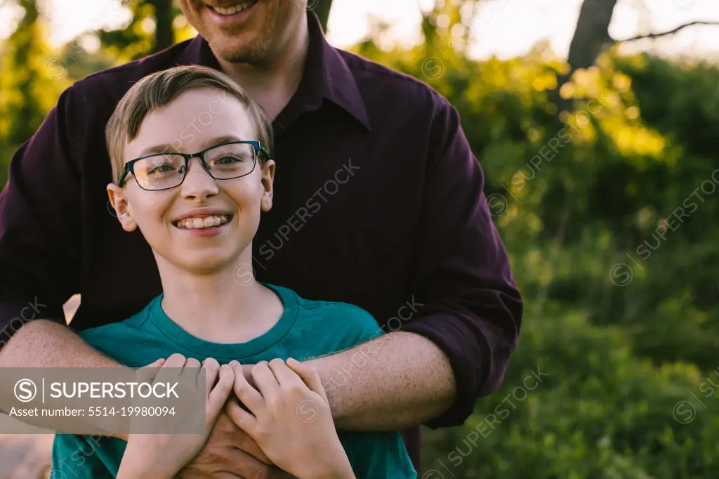 Preteen boy with glasses has happy smile while Dad hugs him