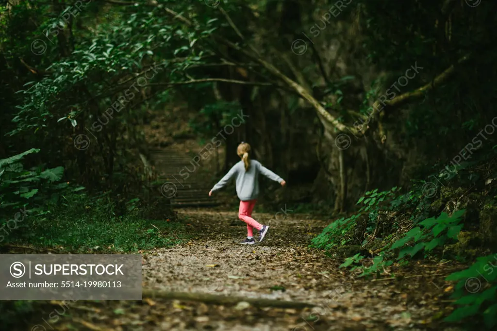 Girl child twirls on path in green forest