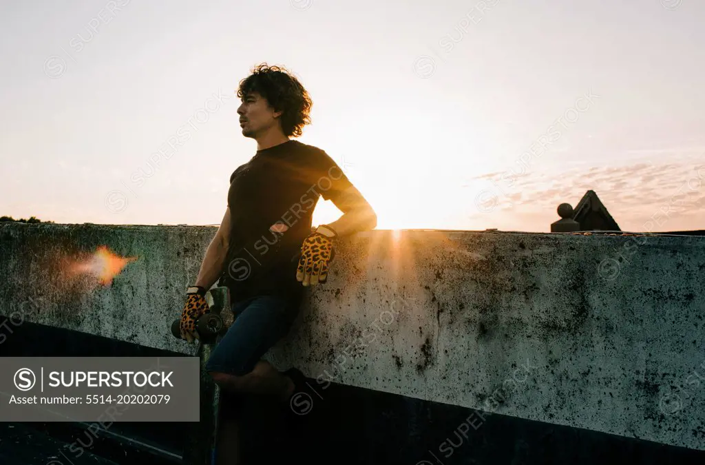 portrait of man standing in the sunset with his skateboard