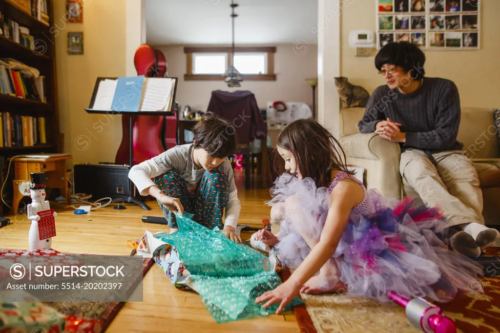 A father looks on while children open Christmas presents