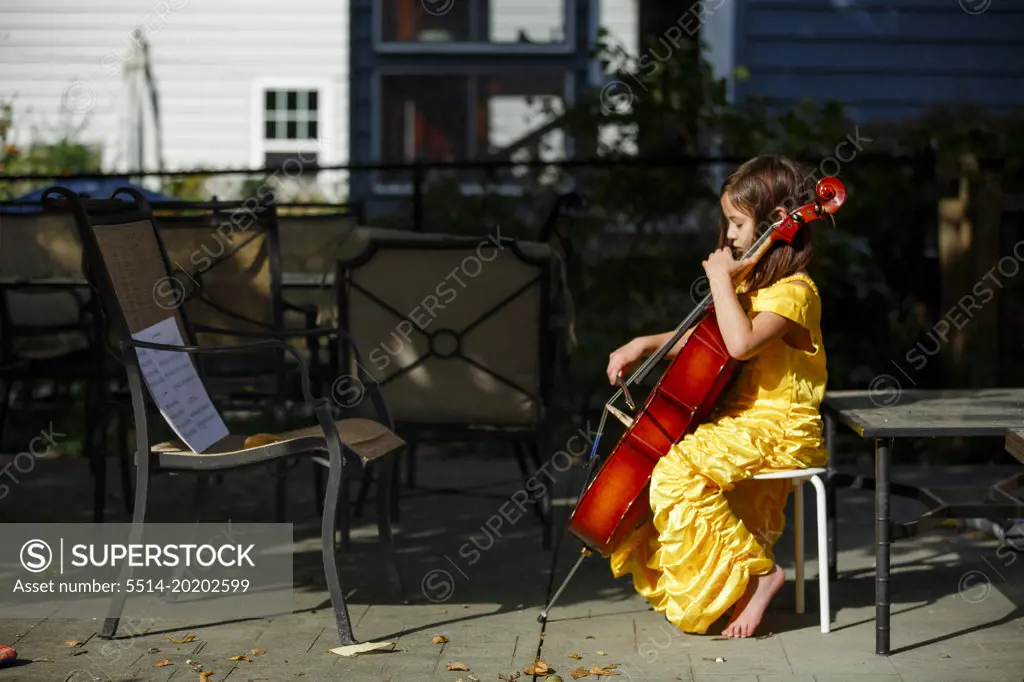 Side-view of focused, barefoot girl playing cello outside in costume