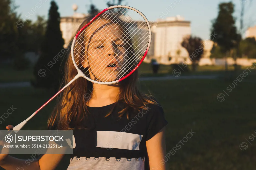 Portrait of girl looking through badminton racket at the park