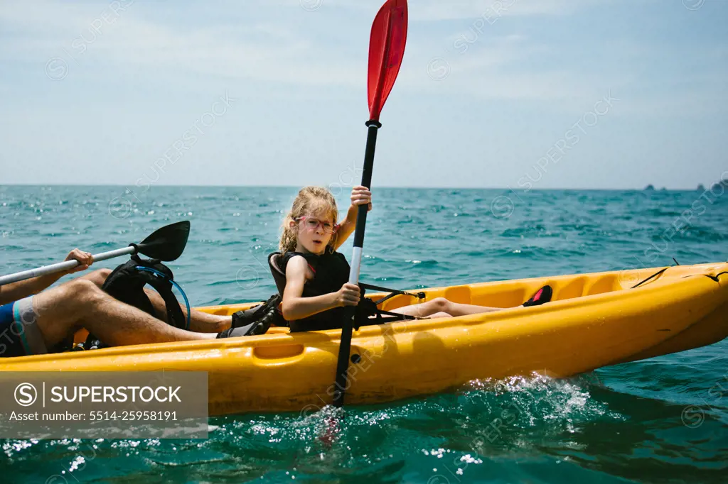 Girl kayaks with her dad on ocean in summer heat