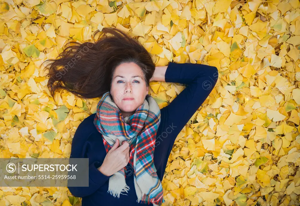 Portrait of a woman laying on a carpet of yellow leaves on autumn day.