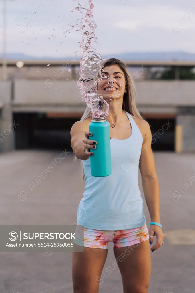 Fitness coach splashing drink out of water bottle outside while 