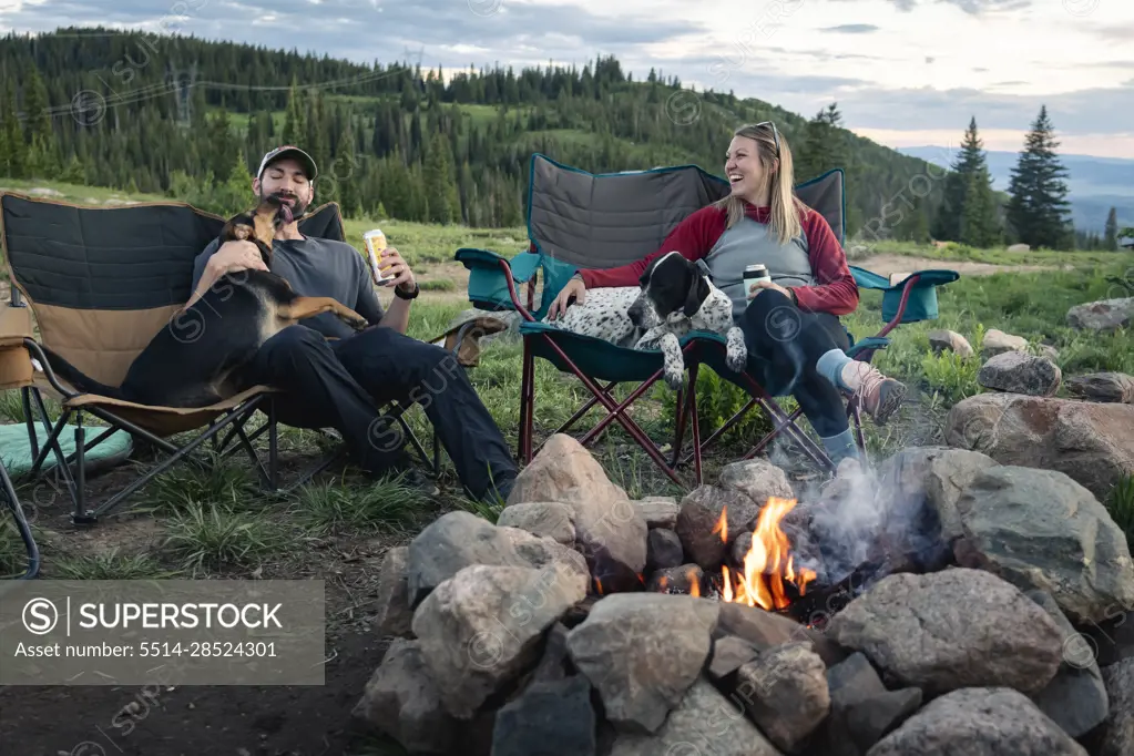 Couple sitting with dogs in chairs at campsite during sunset