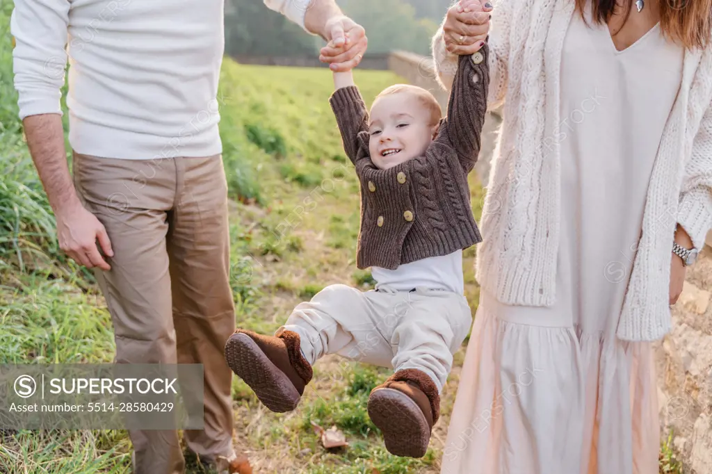 Mom and dad hold the toddler boy by the arms and roll him, he la