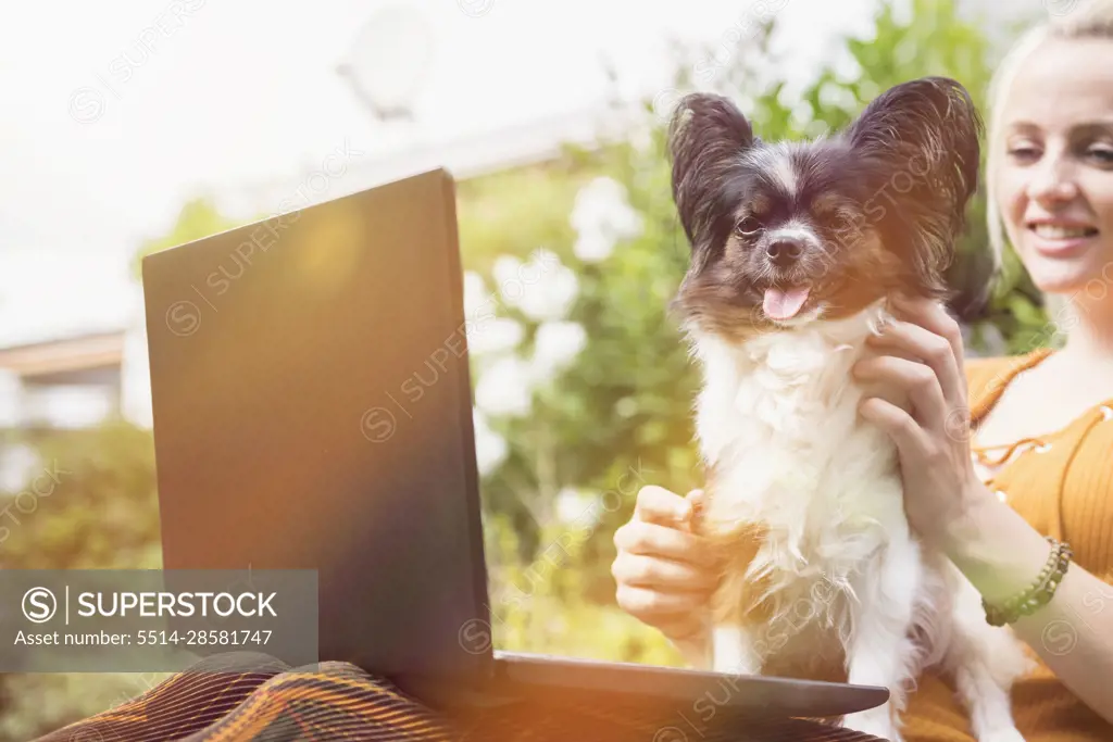 Young woman using laptop with her dog in the domestic garden, Munich, Bavaria, Germany