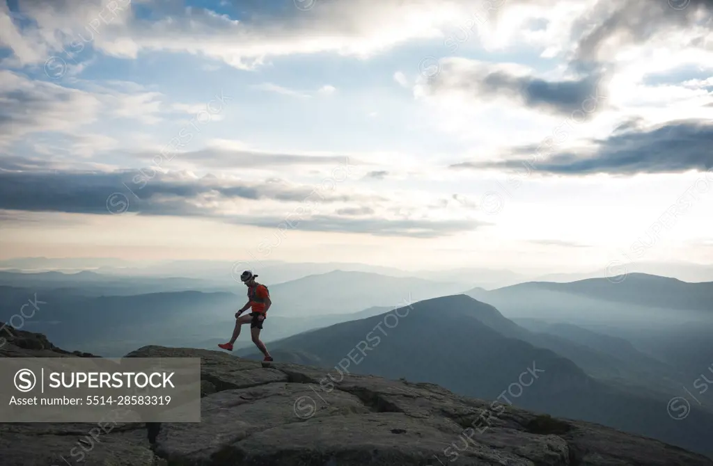 Trail runner man walking along ridge with mountains