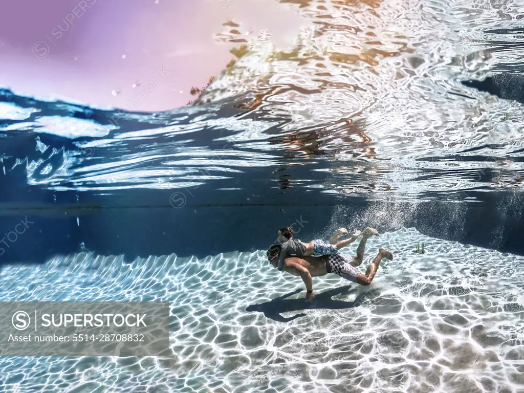 Son holding onto dad swimming underwater in the pool