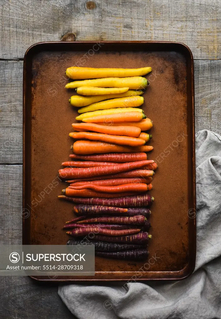 Metal pan of multicoloured carrots on a wooden background.