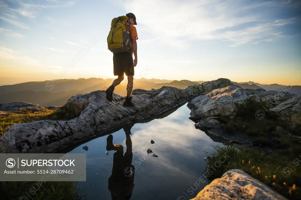 Active man escapes the city, hiking on a summit ridge at sunset.