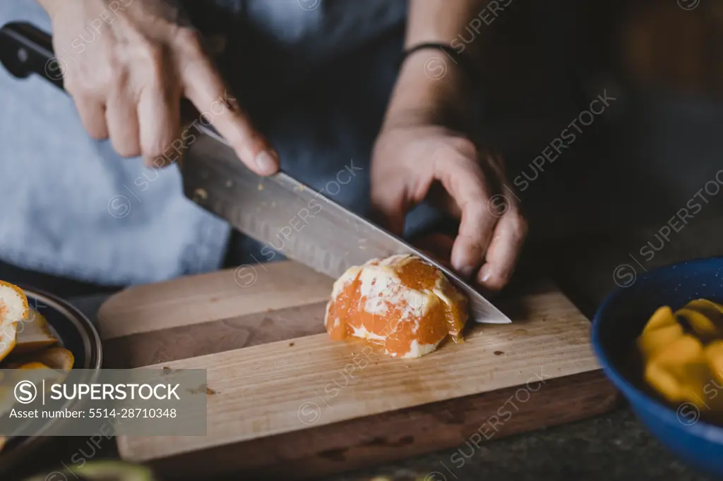 Closeup of hands and knife cutting orange on wooden cutting board