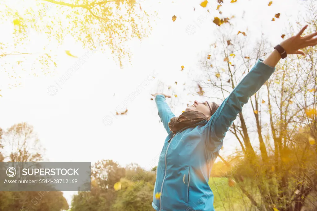 Woman laughing while throwing autumn leaves in air