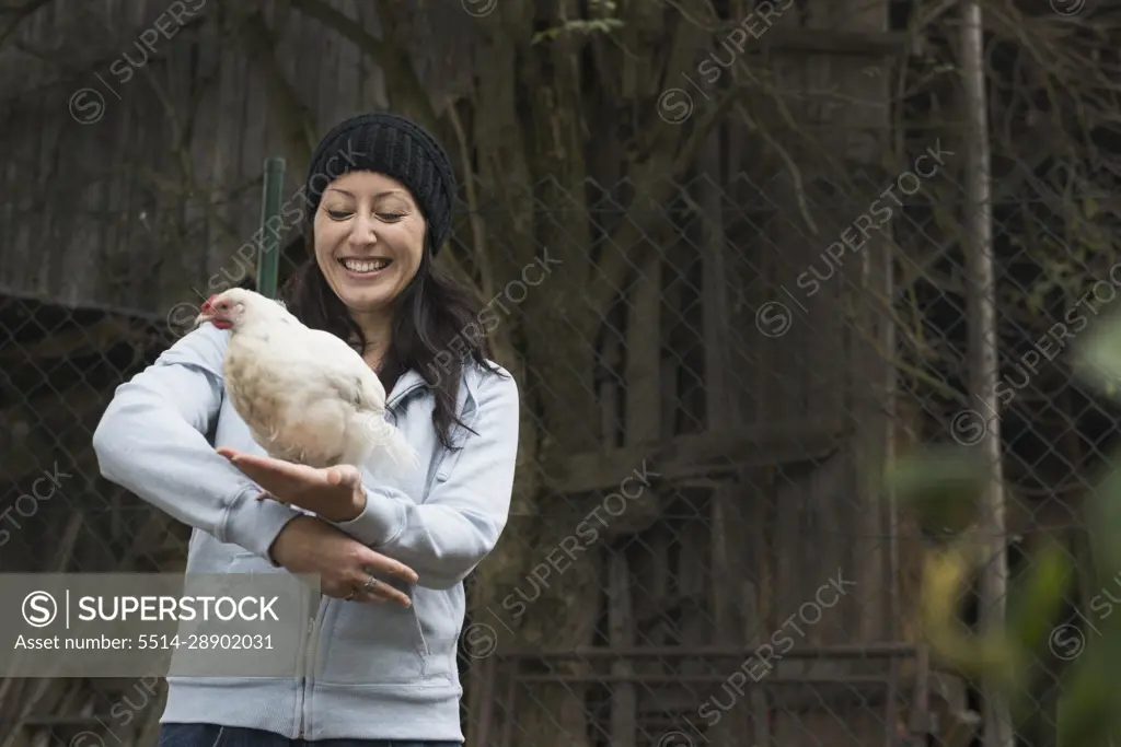 Farmer woman with white chicken bird and smiling in farm, Bavaria, Germany