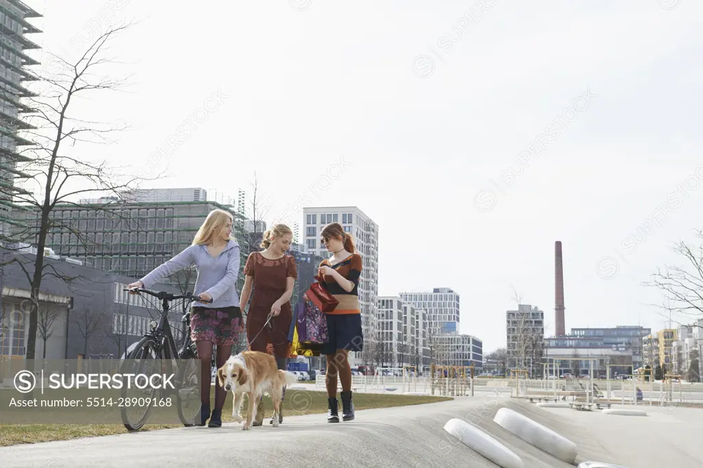 Three friends walking in a playground with dog, Munich, Bavaria, Germany