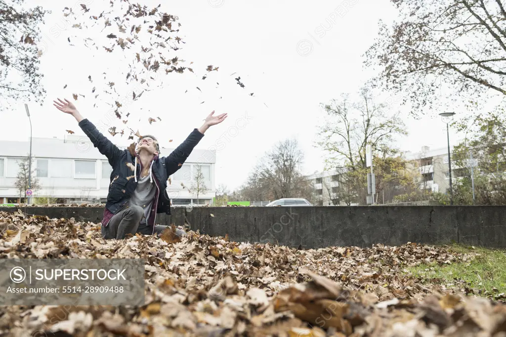 Young man throwing autumn dry leaves in air, Munich, Bavaria, Germany