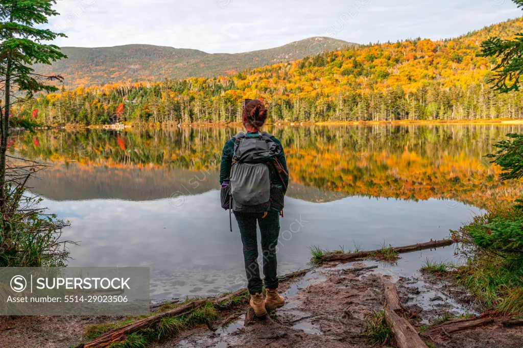 Young woman staring out at colorful trees reflecting in lake water.