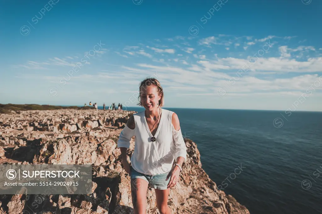 Young woman on cliff looking out over ocean in summer in Portugal