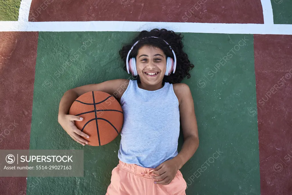 A little girl with curly hair is lying on a basketball court laughing