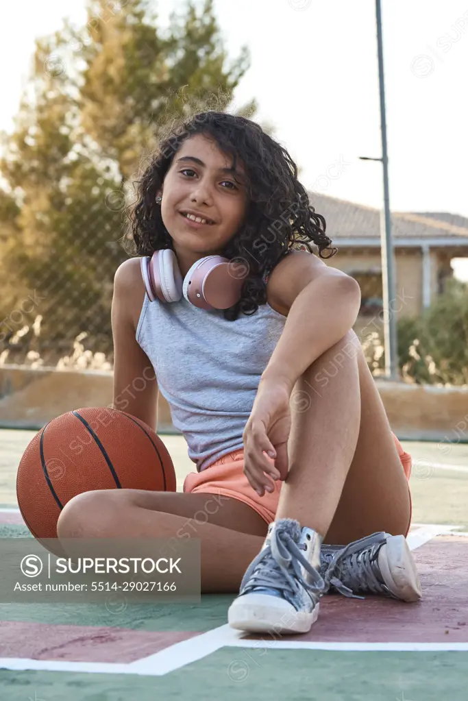 Close-up of a sitting girl with curly hair with a basketball and headphones