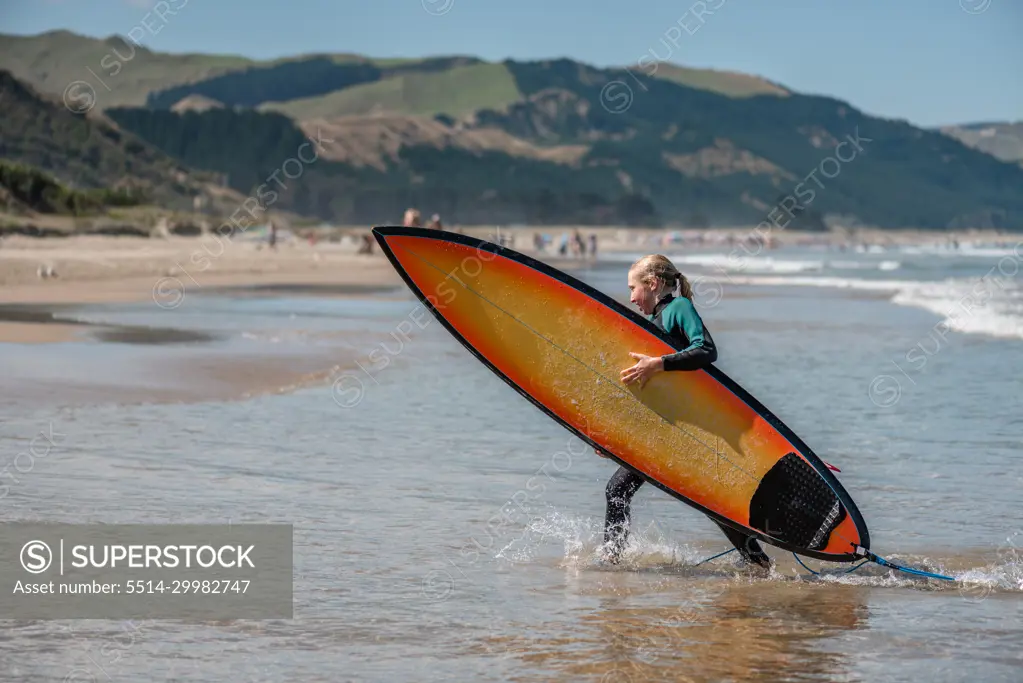 Tween girl carrying a surfboard in New Zealand