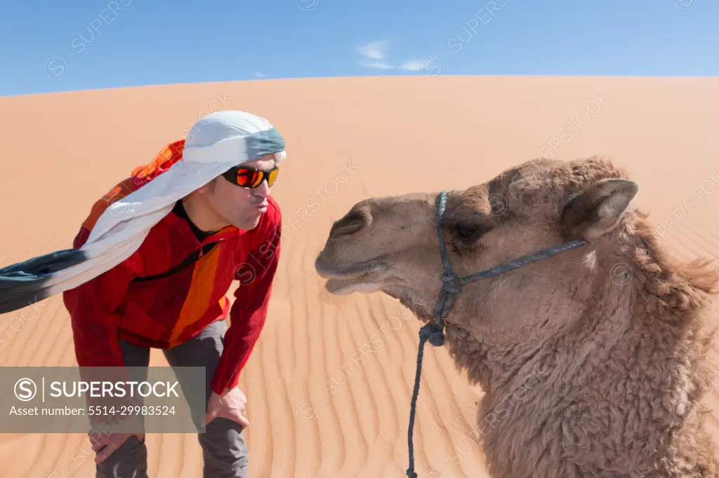 Tourist with turban and sunglasses kissing a camel in the desert dunes