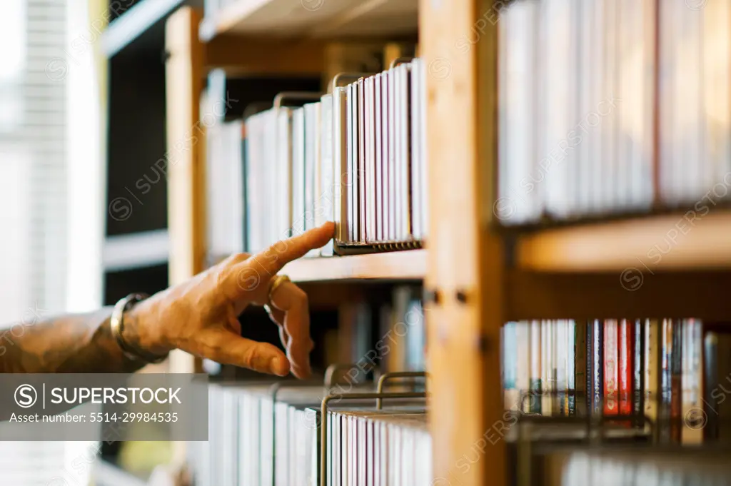 man searching through cds on a bookshelf with his hand