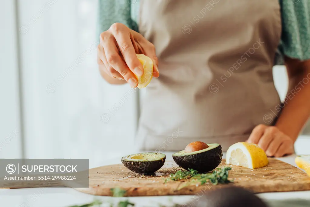 Female hands squeezing lemon on avocado while preparing healthy meal