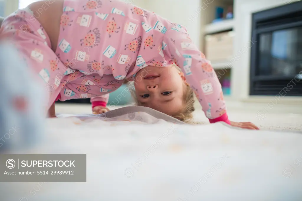 Young girl bend upside down, playing in living room at home.