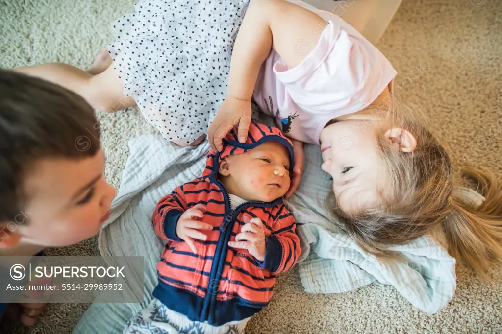 Older brother and sister cuddle their new baby brother.