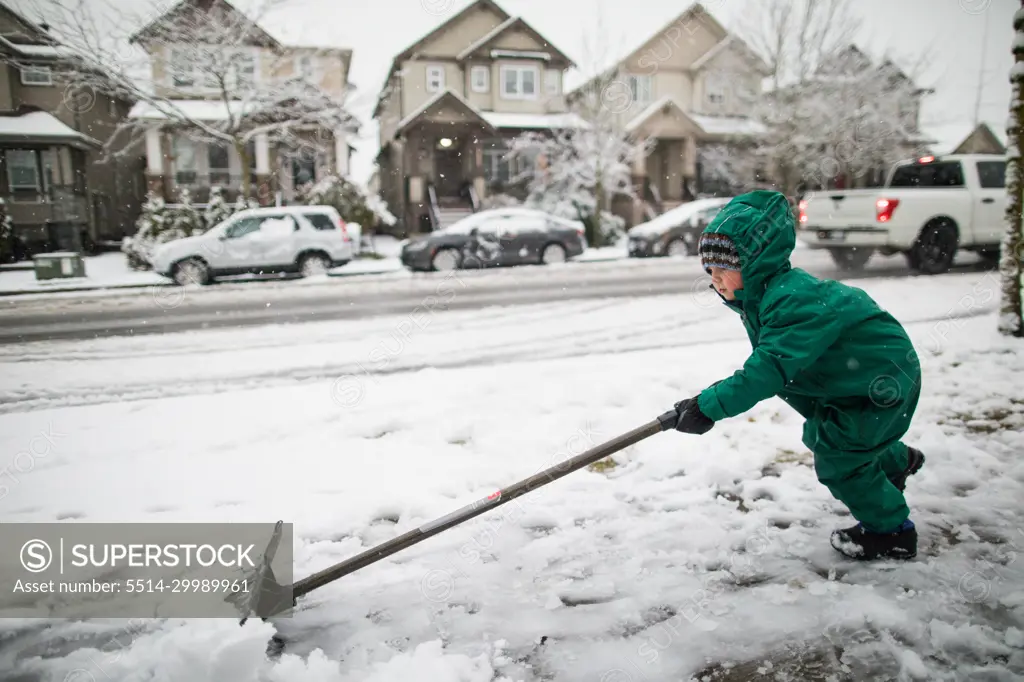 strong young boy shovels, pushes snow off the sidewalk