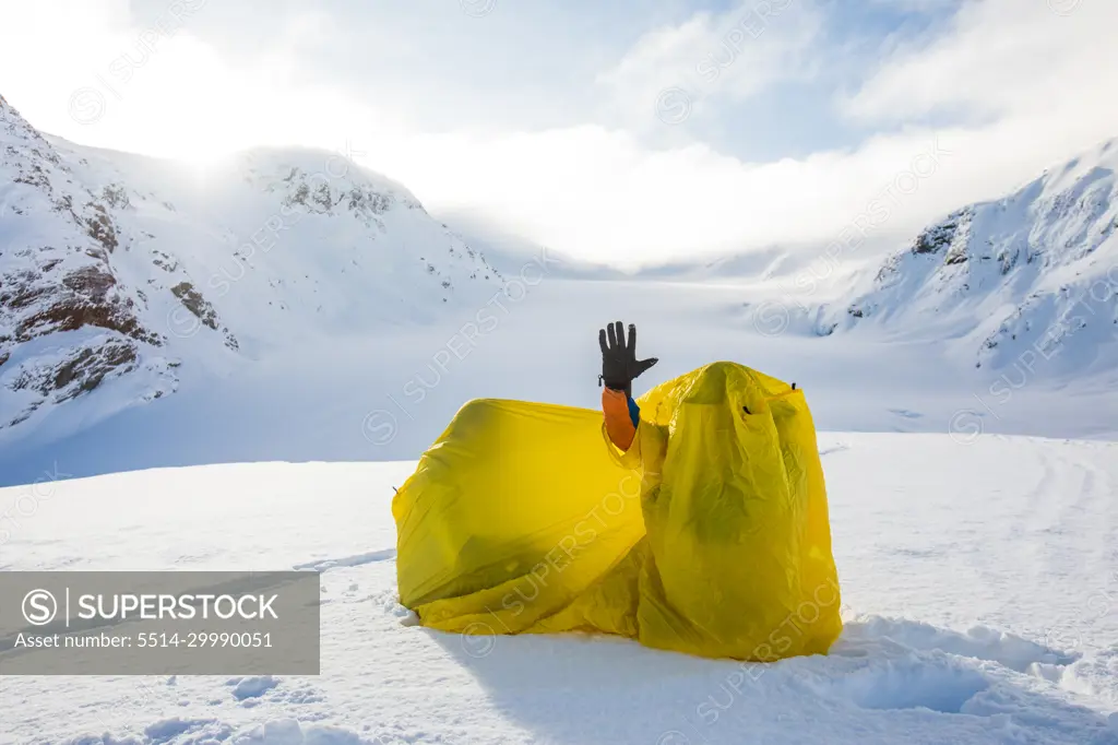 Hand sticking out, waving from inside yellow tent shelter