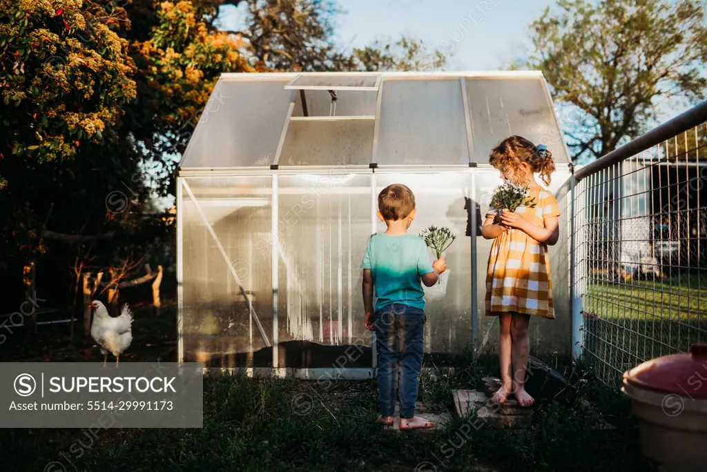 Young kids standing outside backyard green house holding flowers