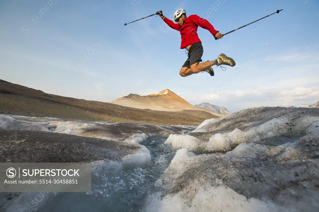 Hiker jumps over glacial stream.