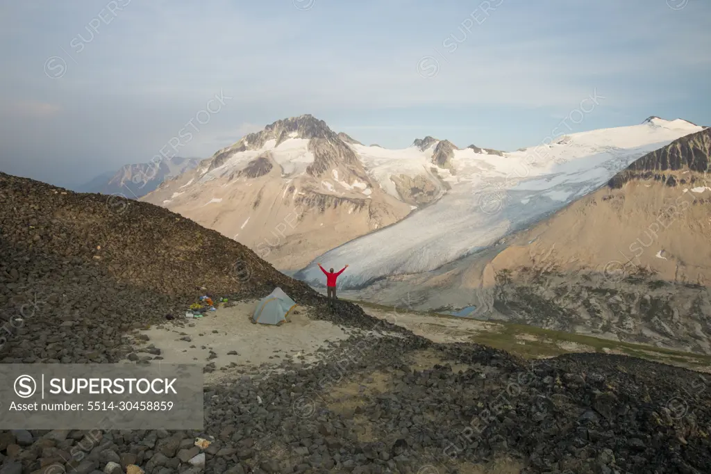 hiker raises hands in the air, overjoyed by view.