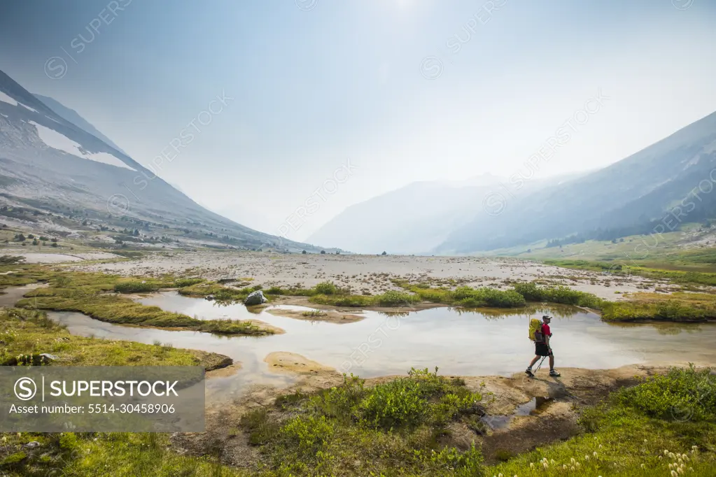 Side view of backpacker hiking next to stream in lush valley.