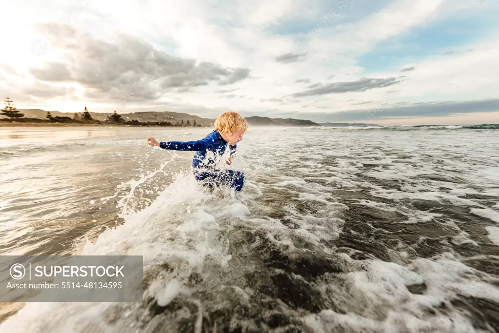 Young child jumping waves at a beach in New Zealand