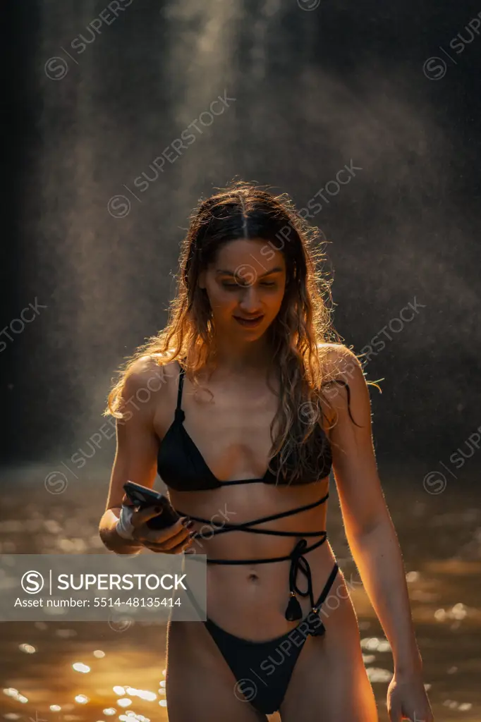 Woman tourist near a waterfall takes a photo on a smartphone.