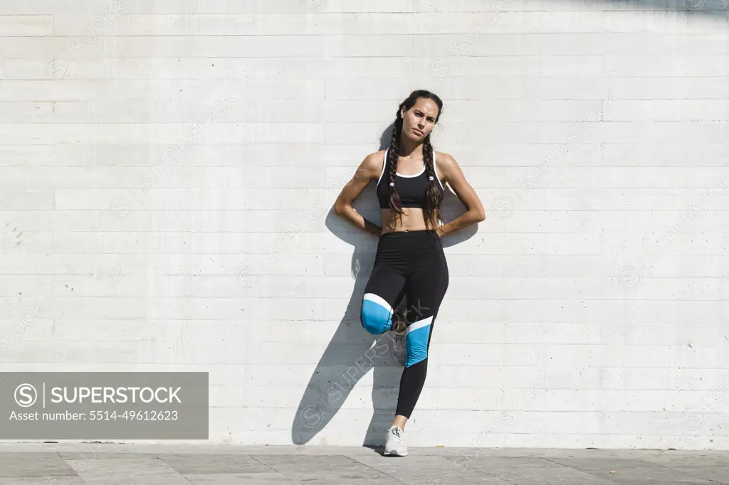 Full body portrait of female athlete leaning on concrete wall