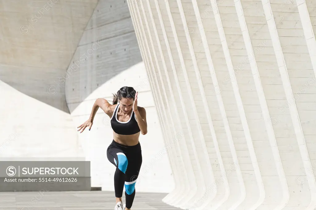 Upper body of female athlete in sportswear running fast on concrete