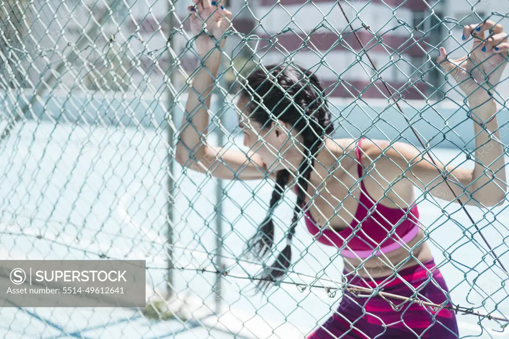 Upper body of female athlete leaning on court fence while resting