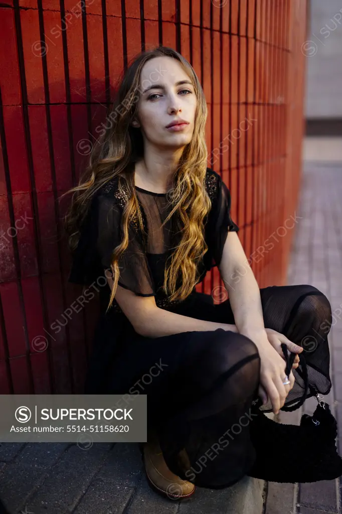 Woman sitting near a red wall in a black dress