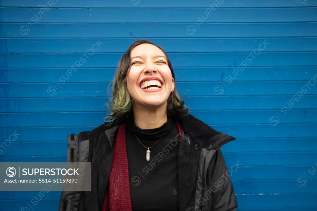 Laughing young woman with closed eyes on blue wall, in rain.