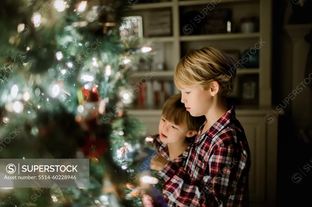 Two boys in plaid pajamas admiring a decorated Christmas tree at