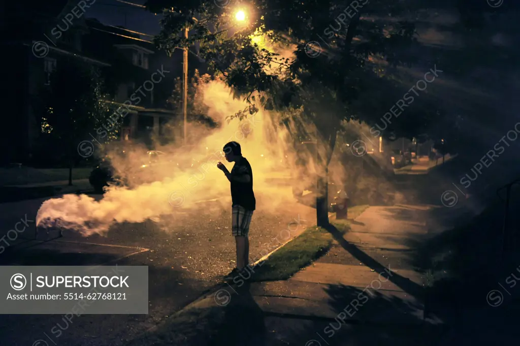 A young boy playing with fireworks in the middle of a neighborhood street