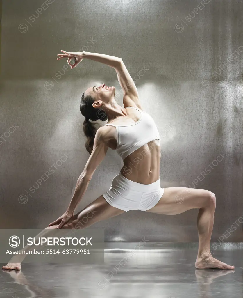 A caucasian female performs yoga in a studio