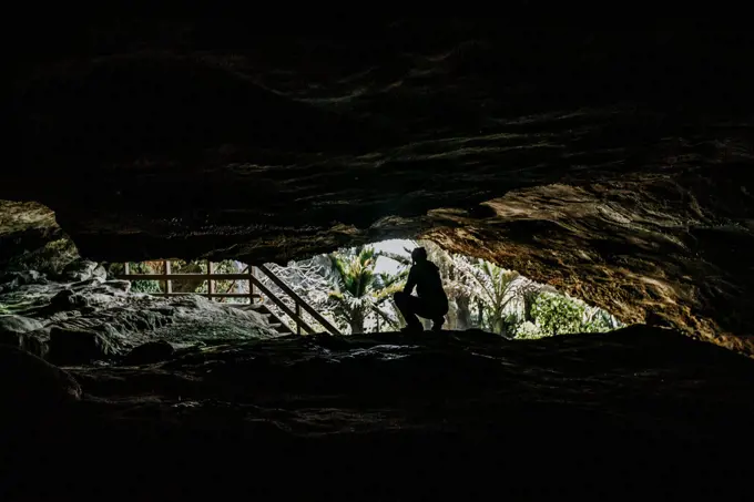 A woman in silhouette kneels at the entrance to a cave in New Zealand