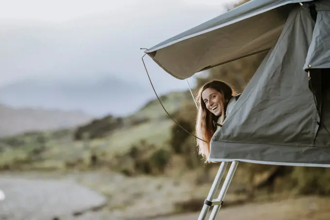 A young smiling woman sticks her head out of a tent in New Zealand.